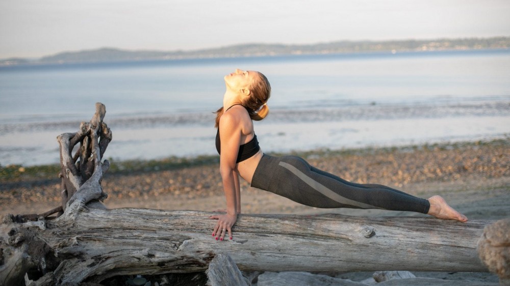 Woman doing upward facing dog on a tree trunk in front of the sea.